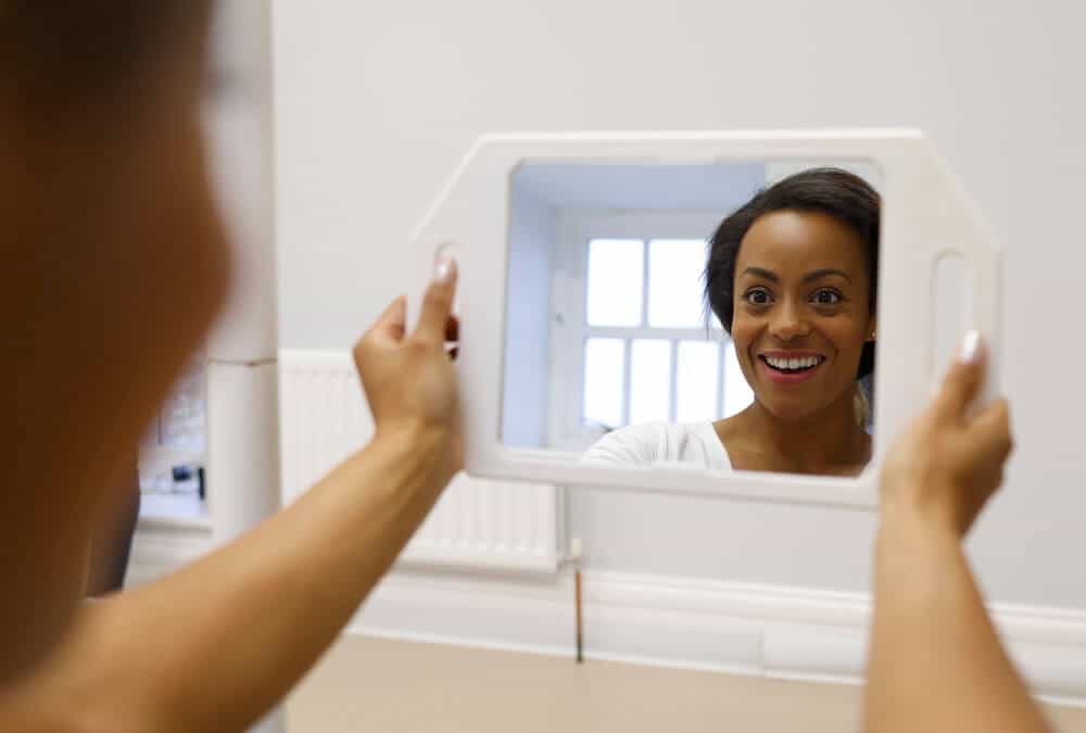 An invisslign patient looks at her smile in the mirror after treatment