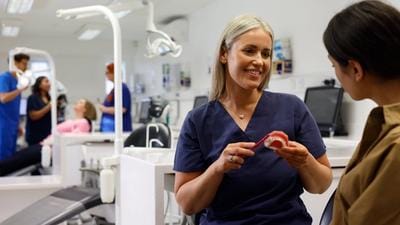 A close up on an orthodontist inspecting a mouth with fixed braces and colourful bracket modules
